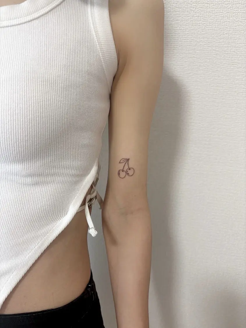 女性の二の腕にあるサクランボのラインタトゥー
